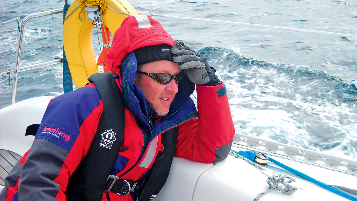 A new boat owner on a shakedown sail on his yacht, wearing red and blue wet weather gear