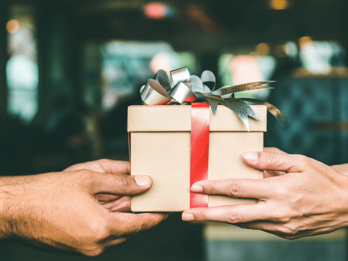 a box wrapped in a ribbon and a festive decoration is passed between female and male hands.