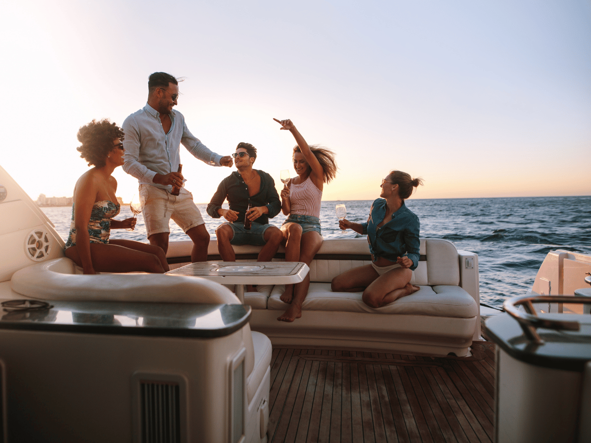 a group of people socialise on deck of a boat. They sit around a table on large upholstered benches